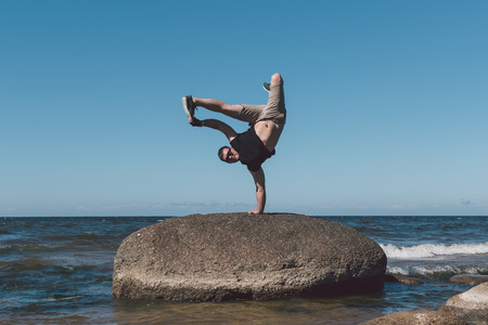 Strong man posing on a stone against a background of a bay and the sky. Photo in the daytime.の写真素材