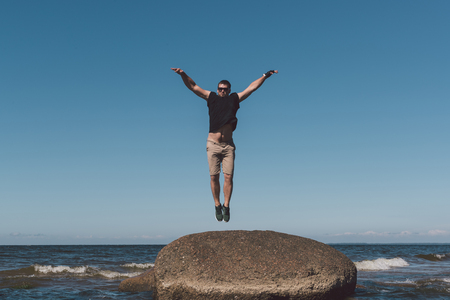 Strong man posing on a stone against a background of a bay and the sky. Photo in the daytime.の写真素材