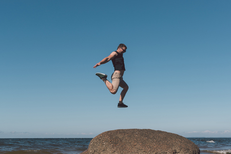 Strong man posing on a stone against a background of a bay and the sky. Photo in the daytime.の写真素材