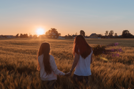 Mom and daughter hold hands and step on the yellow field. Outdoors photo.の写真素材