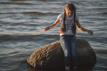 young girl sits on a rock in the seaの写真素材