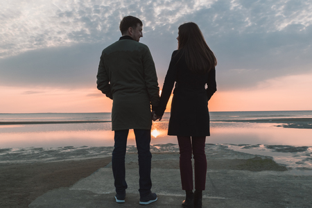 young loving couple holding hands on the seashore in autumn.の写真素材