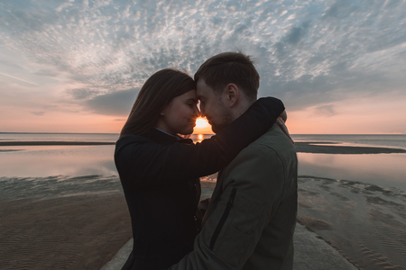 young loving couple hugging on the seashore sunset in autumnの写真素材