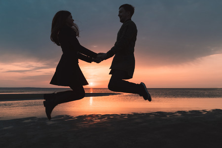 young couple in love jumping at sunset on the beach in autumnの写真素材