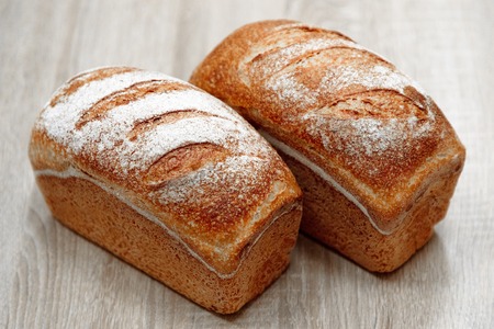 two tasty baked bread on a light wooden backgroundの写真素材