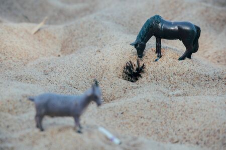 plastic toys in the form of horses and goats on the sand in the daytime