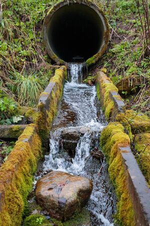 flow of the river through the old drain pipes in the forest in the autumnの写真素材