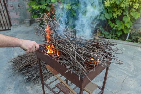 hand adjusts the branches for the fire in the grillの写真素材