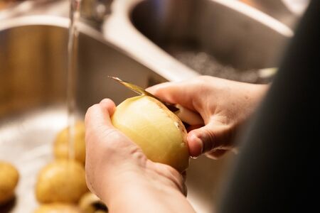 woman peeling potatoes over a sink closeupの写真素材