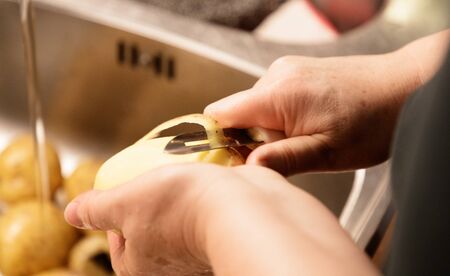 woman peeling potatoes over a sink closeup