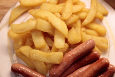 fried potatoes with fried sausages on a plate close up.の写真素材