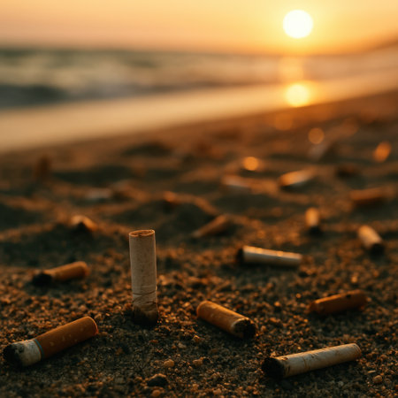 Close up of cigarette butts scattered on sandy beach during sunset. Environmental pollution concept showing impact of smoking waste on nature and oceans.の素材