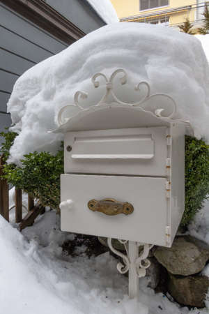 Snow-covered white metal mailbox in the Swiss winter resort of Engelbergの写真素材