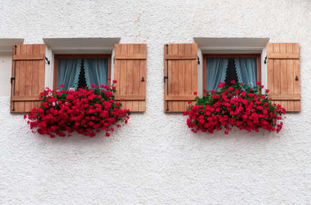 Two identical windows of a house in Samnaun with wooden windows decorated with lush red flowers