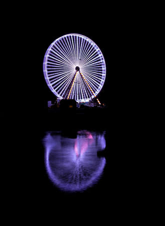 Spinning ferris wheel in Honfleur in the night with its reflection in the sea waterの写真素材