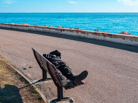 A lone beggar sleeps on a bench by the Mediterranean coast in Menton, Franceの写真素材