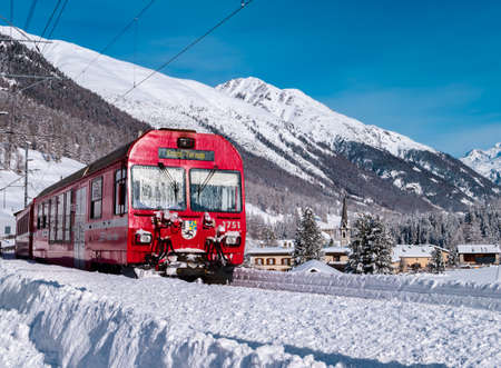 Cinuos-Chel, Switzerland - February 3, 2022: Red train riding between Chur and Tirano in Italy and crossing snow covered landscape at the village Chinous-Chel in Grisons.のeditorial素材