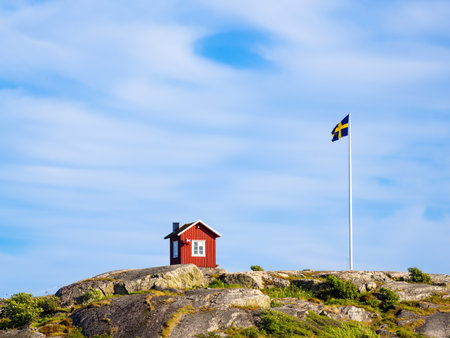 Isolated red swedish wooden cottage and swedish flag on the top of the hill of the island of Vrango in Sweden, near the Gothenburgの写真素材