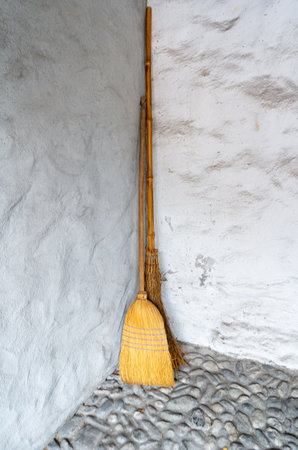 Two obsolete brooms or besoms leaning in the corner of the gray wall