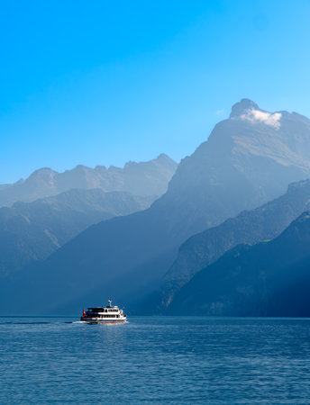Outlines of the mountains by the swiss Lake Urnersee - Lake Luzerne - in the daytime hazy light. Tourist ship on the lake.の写真素材