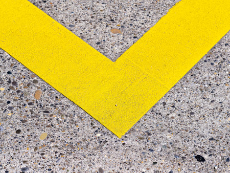 Close-up view of yellow V-shaped line on textured concrete pavement, contrasting colors and...