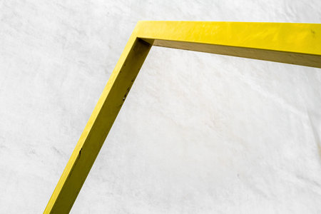 Minimalist image of a yellow metal frame against a white textured wall.の写真素材