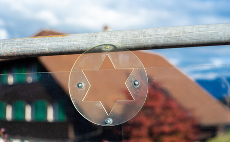 Star of David cutout on a glass panel with blurred background. Swiss traditional house in Spiez.