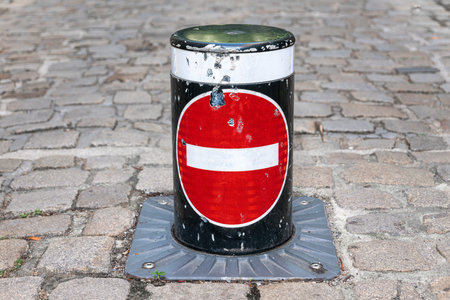 A black and red bollard with a white horizontal bar, set on cobblestone pavementの写真素材