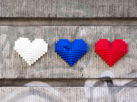 Three pixelated hearts in white, blue, and red arranged on a textured gray wall