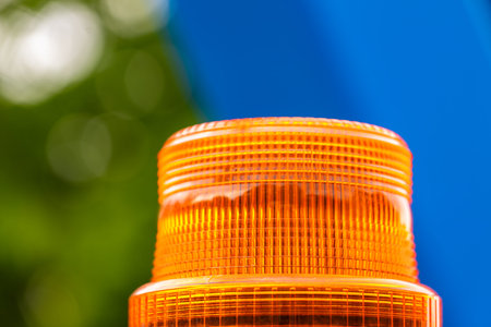 Close-up of an orange warning light against a blurred blue and green background, emphasizing the...