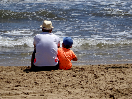 father and son chatting at the seashore on a sandy beach on summer vacationの写真素材