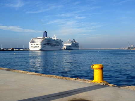 two cruise ships docked at the port face to face on a day with blue sky with a yellow bollardの写真素材