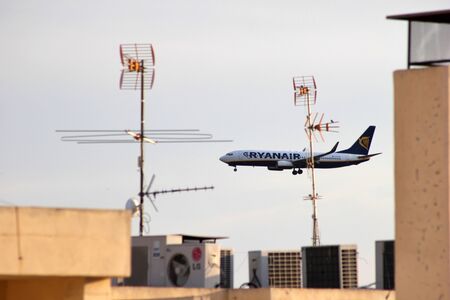 Ryanair passenger aircraft in landing approach to Alicante Airport. View from the terrace of a building with rooftop and TV antennasのeditorial素材