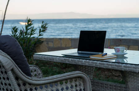 working from summer house remote concept in pandemic, table ready for work with laptop notebook pen phone near the seasideの写真素材