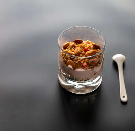 Healthy breakfast. Granola with yogurt and nuts in a glass on a black background