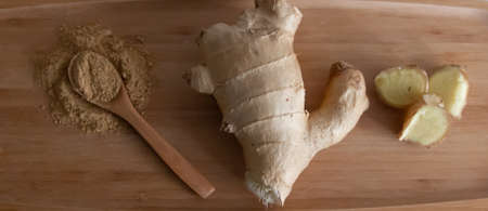 Ginger powder and ginger root on a wooden board, top view