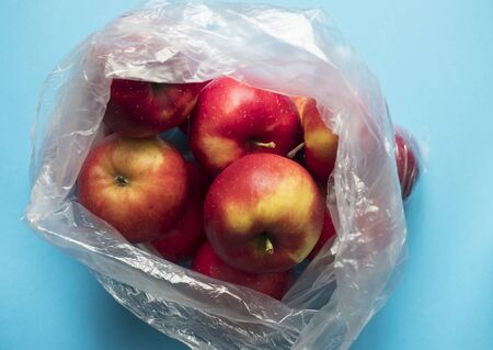 Fresh red apples in a plastic bag on a blue background