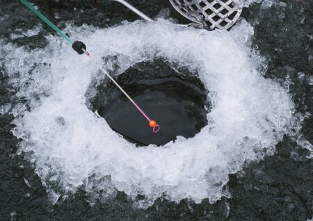 Winter fishing on the lake. A hole in the ice and a fishing rod with a nodの写真素材