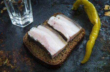 Salted pork bacon on black bread, a glass of vodka and hot pepperの写真素材