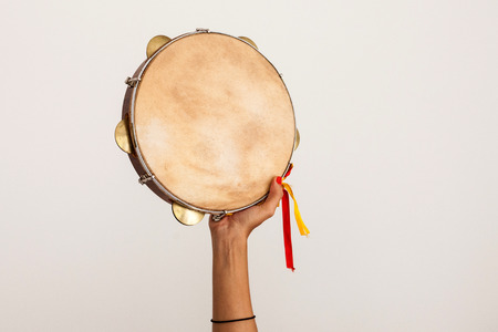 Hand holding tambourine with yellow and red ribbons on white background