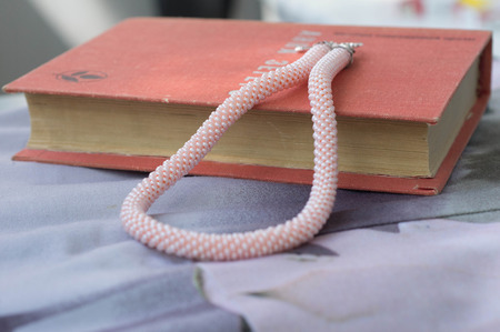 Knitted necklace from beads of pink color on the bookの写真素材