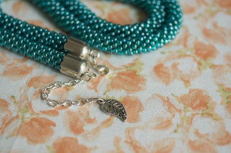 Green-blue necklace from beads against a flower printの写真素材