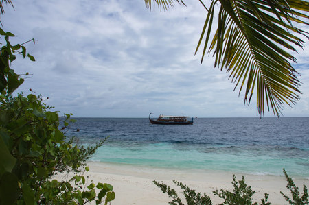 The sandy beach and a boat floating on the ocean in cloudy weatherの写真素材