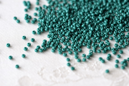 Scattered seed beads of emerald color on the textile backgroundの写真素材
