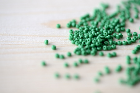 Scattered seed beads of green color on the wooden backgroundの写真素材