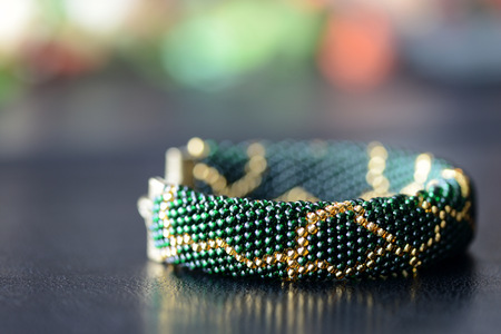 Dark green beaded bracelet with a golden pattern on a dark background