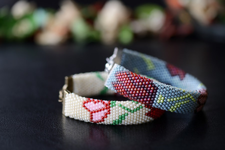 Beige and gray beaded bracelets with flower print on a dark background close up