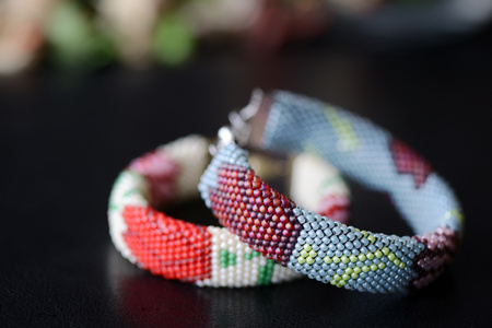 Beige and gray beaded bracelets with flower print on a dark background close upの写真素材