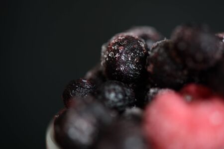Frozen raspberries and blueberries on a dark background close up