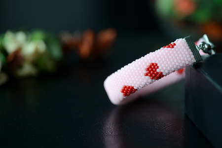 Pink beaded bracelet with images of red hearts on a dark background close up